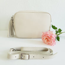 Lataa kuva Galleria-katseluun, ANGIE olkalaukussa on kaksi säädettävää olkahihnaa ja vetoketjukiinnitys. Tupsukoriste toimii vetimenä. Suosittu crossbody malli. Laukussa yski tasku ja pieni avotasku ja tekstiilivuorikangas. Materiaali: nahkaa Väri: luonnonvalkoinen Koko: pituus 20 cm, korkeus 15 cm, syvyys 7 cm.