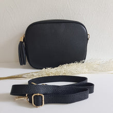 Lataa kuva Galleria-katseluun, BETTIE olkalaukku on aitoa nahkaa. Laukussa on säädettävä olkahihna, vetoketjukiinnitys ja vetoketjullinen takatasku. Tupsukoriste toimii vetimenä. Suosittu crossbody malli. Väri: musta, kullanvärisillä metallilukoilla.