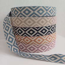 Lataa kuva Galleria-katseluun, Tyylikäs polyesterinauha, josta voi teettää laukku- tai reppuhihnoja, sopii myös vyön valmistukseen. Nauhassa on kaunis kuviointi, pohjaväri on luonnonvalkoinen. Minimitilaus: 1 metri Nauhan leveys: 5 cm Materiaali: 100% polyesteri Värit: sininen, beige, roosa, ruskea ja musta Valmistusmaa: Italia