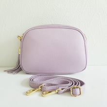 Lataa kuva Galleria-katseluun, Tyylikäs ja tilava LILY crossbody laukku on jaettu kolmeen osastoon. Jokainen osasto suljetaan vetoketjulla. Laukun takaa löytyy vetoketjullinen piilotasku ja sisällä on yksi vetoketjullinen sivutasku. Säädettävä olkahihna, kullanväriset metalliosat. Väri: vaalea lila