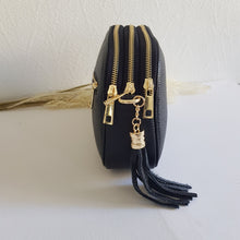 Lataa kuva Galleria-katseluun, Tyylikäs ja tilava LILY crossbody laukku on jaettu kolmeen osastoon. Jokainen osasto suljetaan vetoketjulla. Laukun takaa löytyy vetoketjullinen piilotasku ja sisällä on yksi vetoketjullinen sivutasku. Säädettävä olkahihna, kullanväriset metalliosat. Väri: musta Koko: pituus 23 cm, korkeus 16.6 cm, syvyys 7 cm Olkahihna: leveys 1.5 cm, max pituus 135 cm. Leveä koristeellinen polyesteri/ nahka hihna kullanvärisillä pistolukoilla, leveys 5,5 cm, säädettävä pituus max. 128 cm