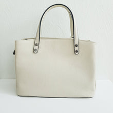 Lataa kuva Galleria-katseluun, Tilava BELINDA nahkalaukku on tyylikäs ja ajaton, suunniteltu klassiseen tyyliin. Laukussa on kaksi pyöristettyä kantokahvaa ja mukana on myös irrotettava, ohut olkahihna, jonka avulla laukkua voi kantaa olkapäällä tai crossbody-tyyliin. Laukussa on kolme erillistä osastoa: keskellä iso vetoketjullinen osasto ja sen molemmilla puolilla osastot magneettilukituksella. Sisältä löytyy lisäksi pieni vetoketjullinen sivutasku ja kaksi pientä avotaskua. Väri: luonnonvalkoinen, tummanhopeat (gunmetal) metalliosat