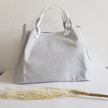 Lataa kuva Galleria-katseluun, Upea CHIARA laukku on tunnetun Bottega Veneta brändin inspiroima malli. Tyylikäs ja tilava laukku on valmistettu aidosta intrecciato punotusta nahasta. Sisällä on vetoketjullinen tilanjakaja sekä vetoketjullinen sivutasku sekä avotasku. Väri: valkoinen Kantokahvat ja olkahihna on säädettävät. Koko: korkeus 32 cm, leveys 50 cm, syvyys 19 cm Olkahihnan koko: leveys 2 cm, max pituus 125 cm Valmistettu Italiassa.