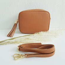 Lataa kuva Galleria-katseluun, ANGIE olkalaukussa on kaksi säädettävää olkahihnaa ja vetoketjukiinnitys. Tupsukoriste toimii vetimenä. Suosittu crossbody malli. Materiaali: aitoa nahkaa Väri: konjakinruskea Koko: pituus 20 cm, korkeus 15 cm, syvyys 7 cm. Laukkuun kuuluu kaksi säädettävää olkahihnaa