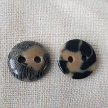 Lataa kuva Galleria-katseluun, Tyylikäs läpiommeltava koristeellinen nappi. Nappi on polyesteria ja napin pintaan on laseroitu abstrakti beige kuviointi. Nappi sopii hyvin villakangastakkeihin, turkistakkeihin, paksuihin neuleisiin ja jakkuihin. Väri on musta/ beige/ harmaa meleeraus. Koot 20 mm (paksuus 7 mm), 25 mm (paksuus 6 mm), 30 mm (paksuus 8 mm).