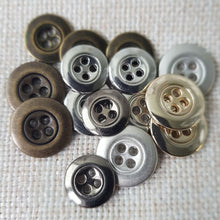 Lataa kuva Galleria-katseluun, Kaunis pieni nelireikäinen metallinappi, jota sanotaan Mari-napiksi. Napin nimitys tulee Marimekon käyttämistä napeista. Tämä on todella ohut metallinappi, jota käytetään hameissa, housuissa, paitapuseroissa ja taskunappina. Käy myös piilonapitukseen. Koot 13 mm ja 15 mm. Värit matta hopea, kirkas hopea, kulta, messinki ja tumma hopea.