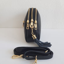 Lataa kuva Galleria-katseluun, Tyylikäs ja tilava LILY crossbody laukku on jaettu kolmeen osastoon. Jokainen osasto suljetaan vetoketjulla. Laukun takaa löytyy vetoketjullinen piilotasku ja sisällä on yksi vetoketjullinen sivutasku. Säädettävä olkahihna, kullanväriset metalliosat. Väri: musta
