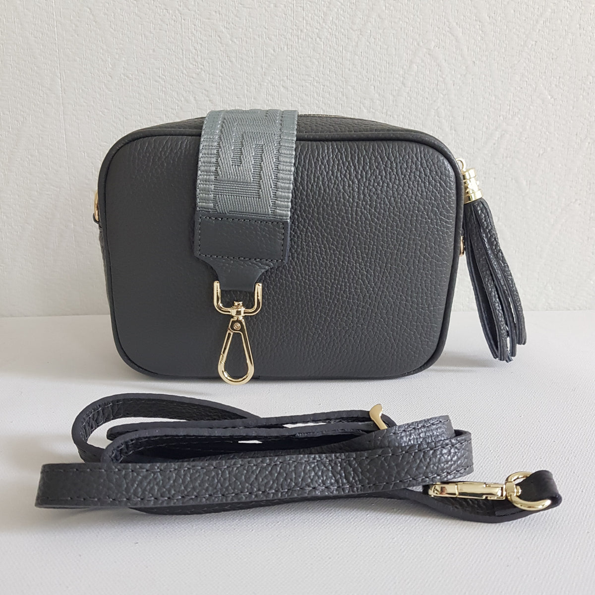 ANGIE olkalaukku on aitoa nahkaa. Laukussa on kaksi säädettävää olkahihnaa ja vetoketjukiinnitys. Tupsukoriste toimii vetimenä. Suosittu crossbody malli.  Väri: tummanharmaa  Koko: pituus 20 cm, korkeus 15 cm, syvyys 7 cm.   Laukkuun kuuluu kaksi säädettävää olkahihnaa:  kapea nahkahihna kullanvärisillä pistolukoilla, leveys 2 cm, säädettävä pituus 128 cm leveä koristeellinen polyesteri/nahka hihna kullanvärisillä pistolukoilla, leveys 5,5 cm, säädettävä pituus max. 128 cm