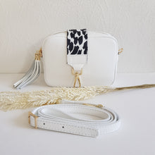 Lataa kuva Galleria-katseluun, ANGIE olkalaukussa on kaksi säädettävää olkahihnaa ja vetoketjukiinnitys. Tupsukoriste toimii vetimenä. Erittäin suosittu crossbody malli.  Materiaali: aitoa nahkaa  Väri: valkoinen  Koko: pituus 20 cm, korkeus 15 cm, syvyys 7 cm.  Laukkuun kuuluu kaksi säädettävää olkahihnaa:  kapea nahkahihna kullanvärisillä pistolukoilla, leveys 2 cm, säädettävä pituus 128 cm leveä koristeellinen polyesteri/nahka hihna kullanvärisillä pistolukoilla, leveys 5,5 cm, säädettävä pituus max. 128 cm
