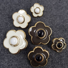 Lataa kuva Galleria-katseluun, Kannallinen muovinen KUKKA koristenappi. Napissa on kullanvärinen pohja kahdella värivaihtoehdolla: luonnonvalkoinen emali/ valkoinen keskus tai ruskea emali/ musta keskus. Koot 18 mm, 23 mm, 28 mm.
